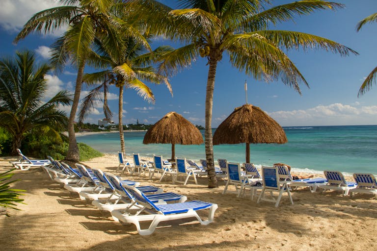 Idyllic beach scene in Akumal, Mexico with sun loungers and palm trees.