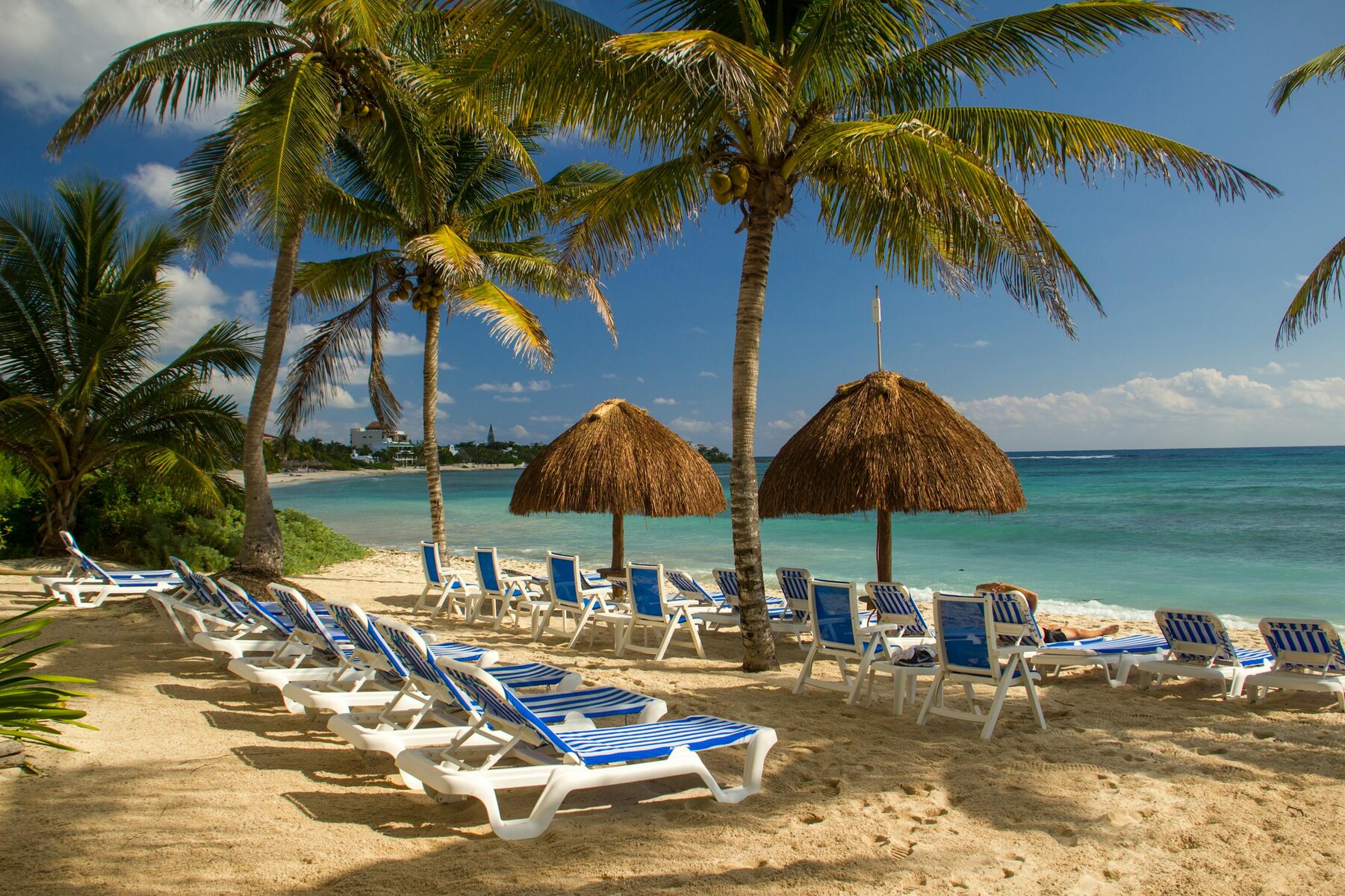 Idyllic beach scene in Akumal, Mexico with sun loungers and palm trees.