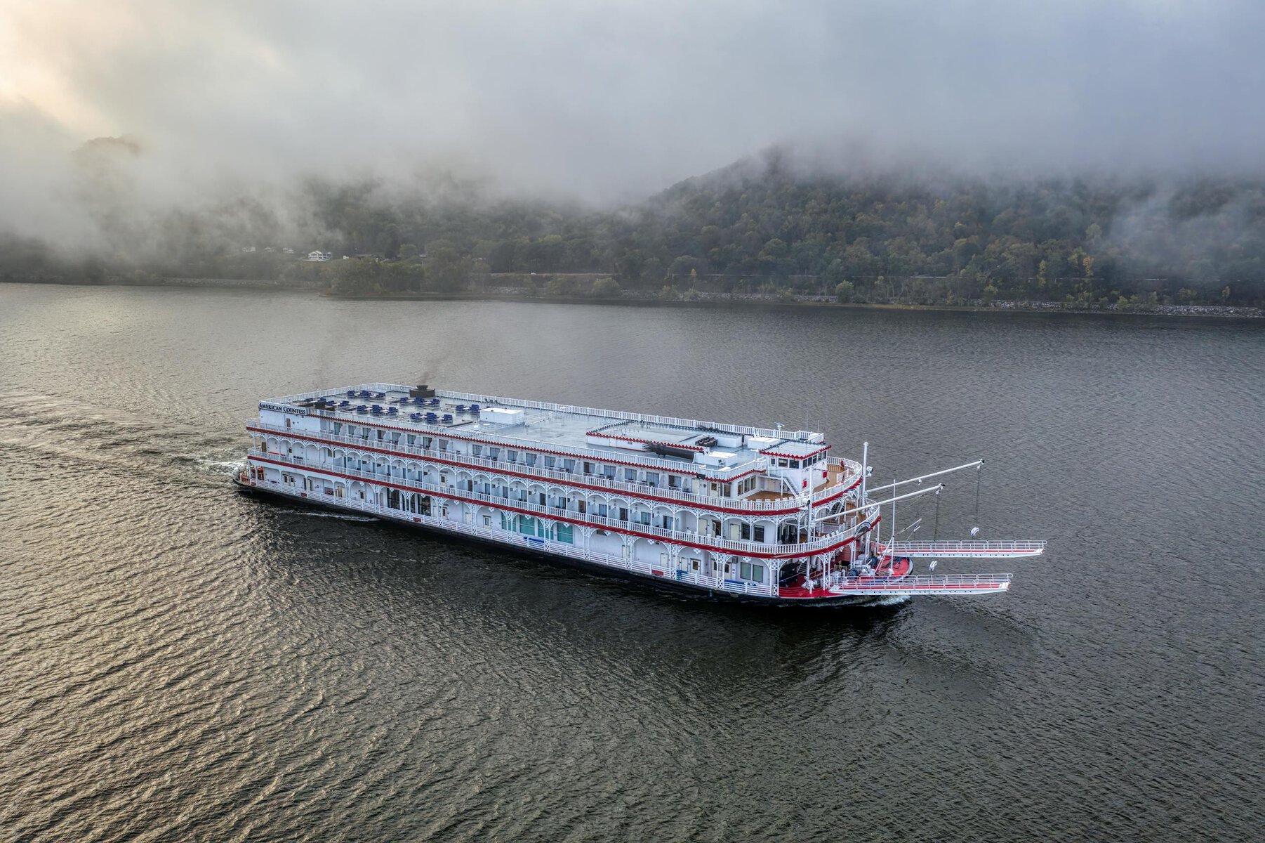 Aerial view of a vintage steamboat cruising through a fog-covered river.